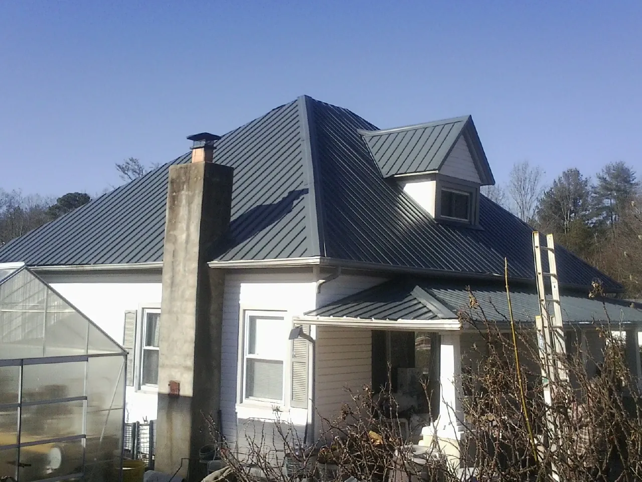 Dark blue standing seam metal roof on a white farmhouse with dormer — Slate & Tile Roof Repair by Roofing Brothers in Mustang