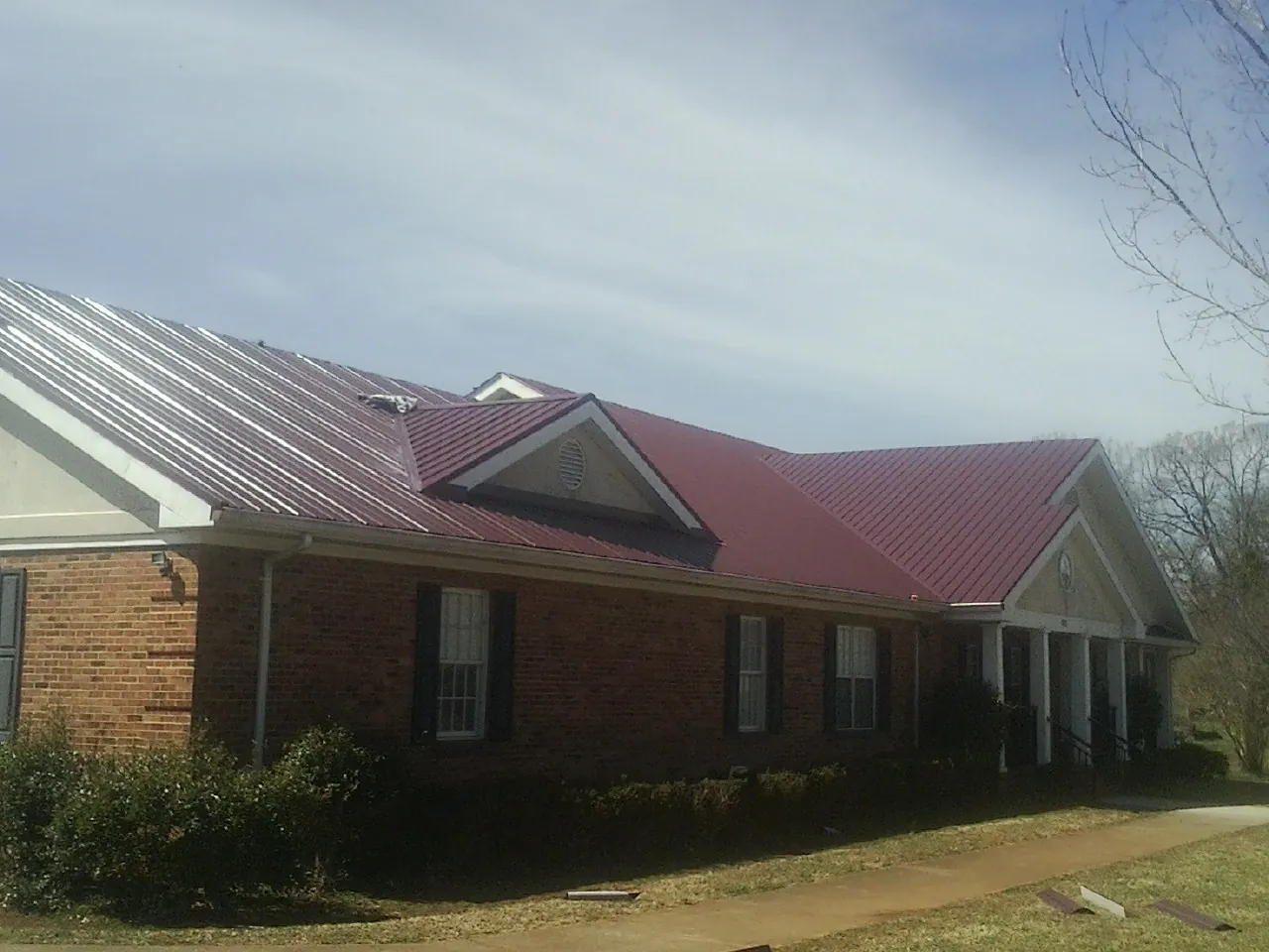 Red metal roof with gabled entries on a long brick building, from a Hail Damage Roof Repair job in Mustang