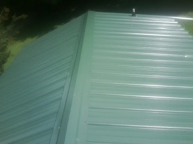 New green metal panels meeting at the ridge of a roof — Flat Roof Repair work by our crew in Mustang
