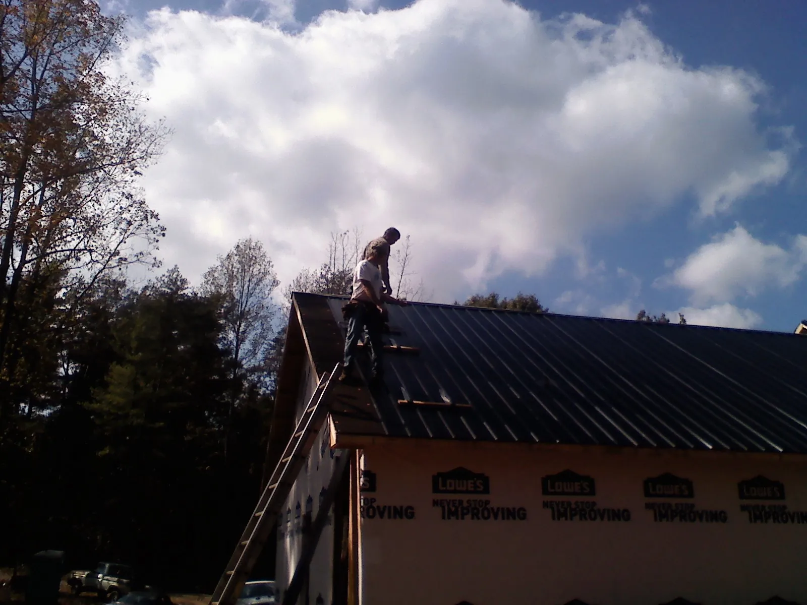 Roofer fastening dark metal panels high against a cloudy sky, from a Roof Inspection job in Mustang