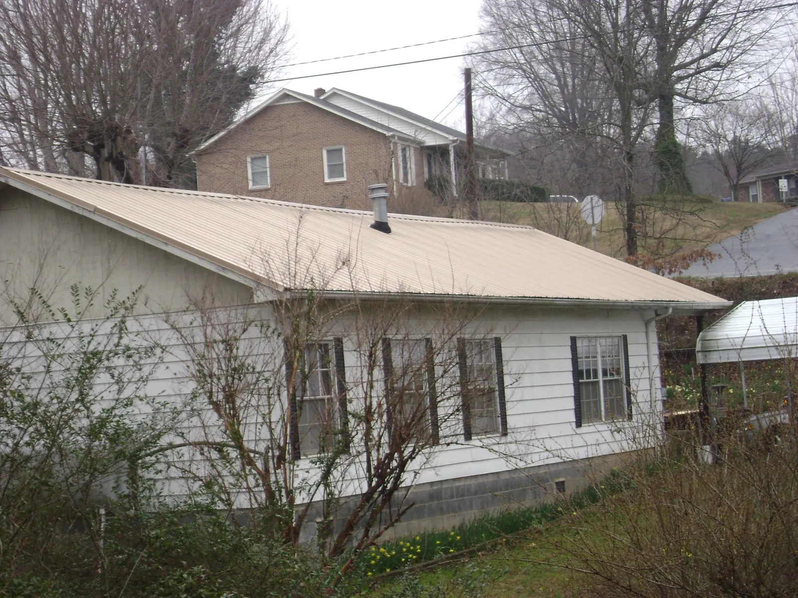 Tan metal roof on a white sided house set into a hillside — Commercial Roofing by Roofing Brothers in Mustang