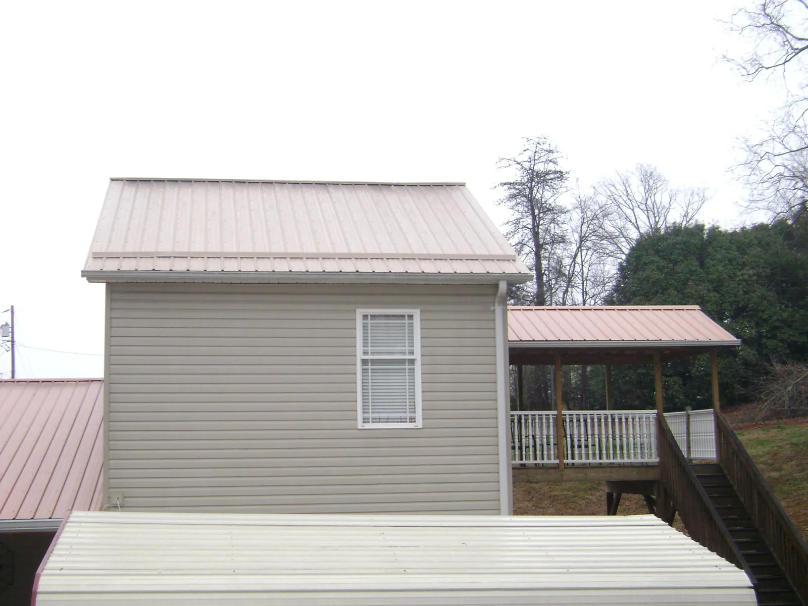 Tan metal roofs on a two story addition and attached porch, from a Roof Replacement job in Mustang